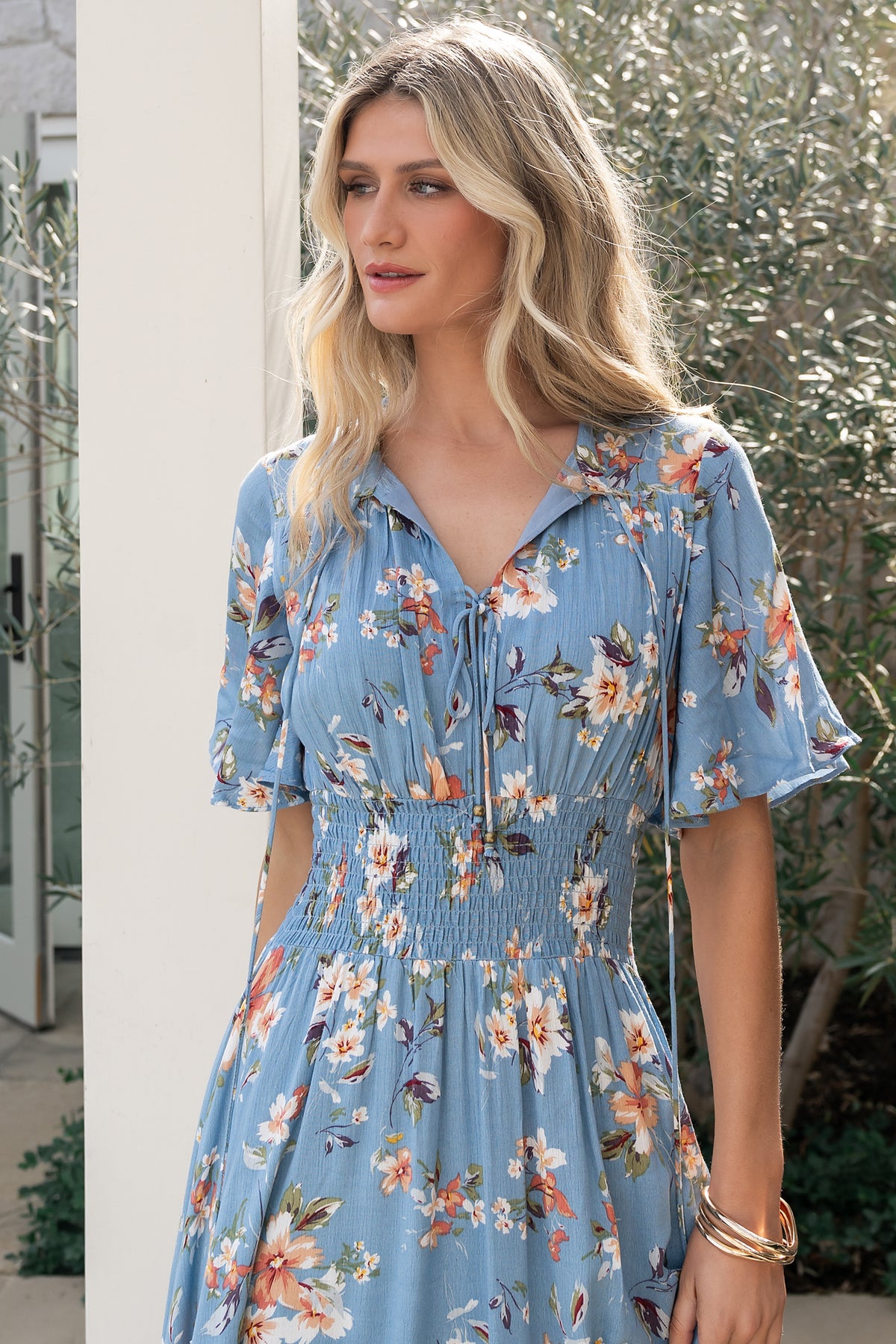 Side view of blue and peach floral midi dress on model, showing gathered shoulder yoke, short sleeves, open-seamed bodice and flowing skirt.