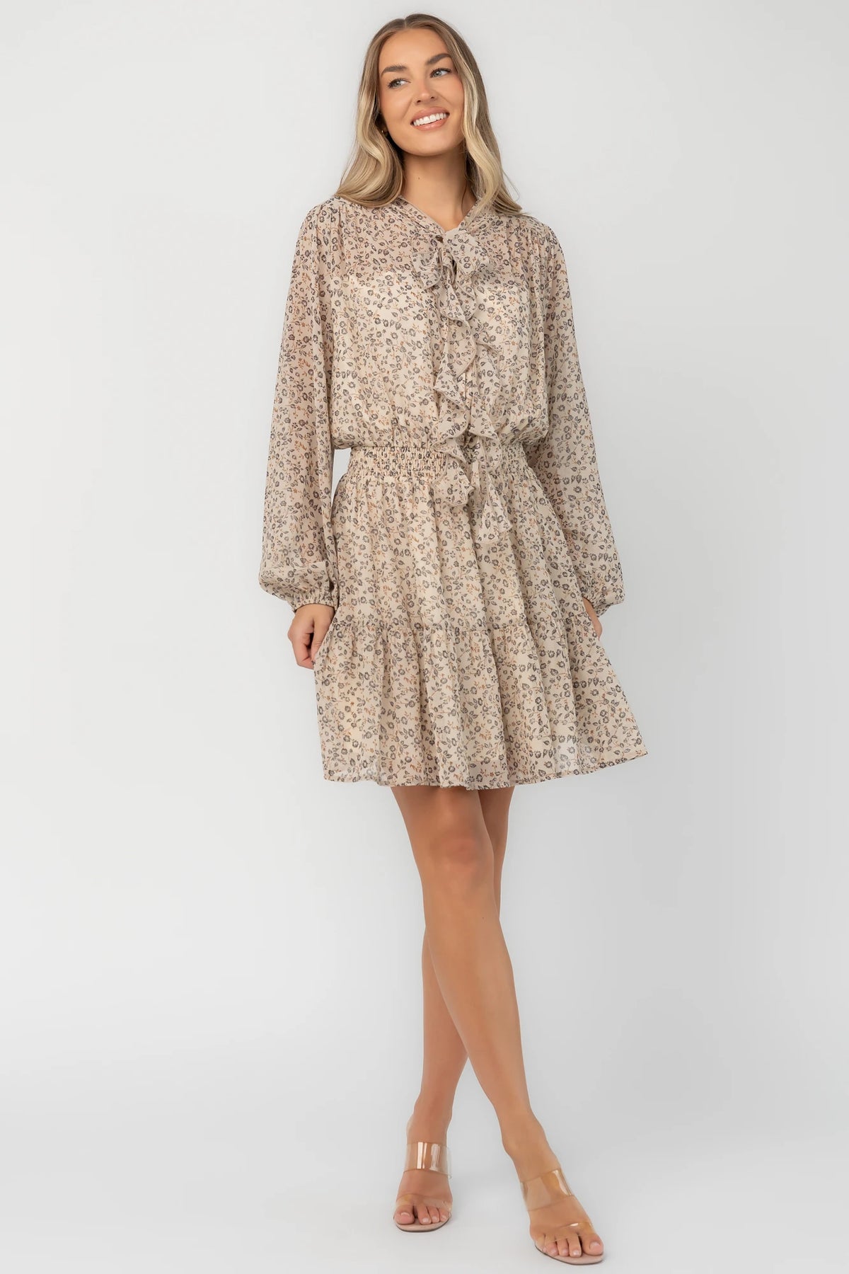 Cream floral mini dress with a self-tie neckline, cascading ruffle detail, long balloon sleeves, smocked waist, and tiered skirt.