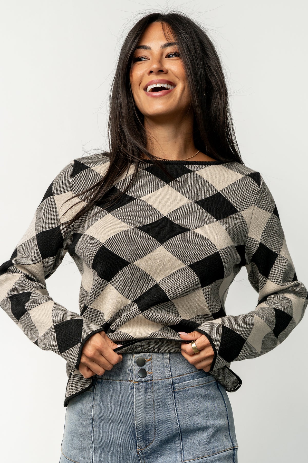 Studio flat-lay showing folded Linnea argyle sweater in black and natural, highlighting pattern symmetry, ribbing, and fabric drape.