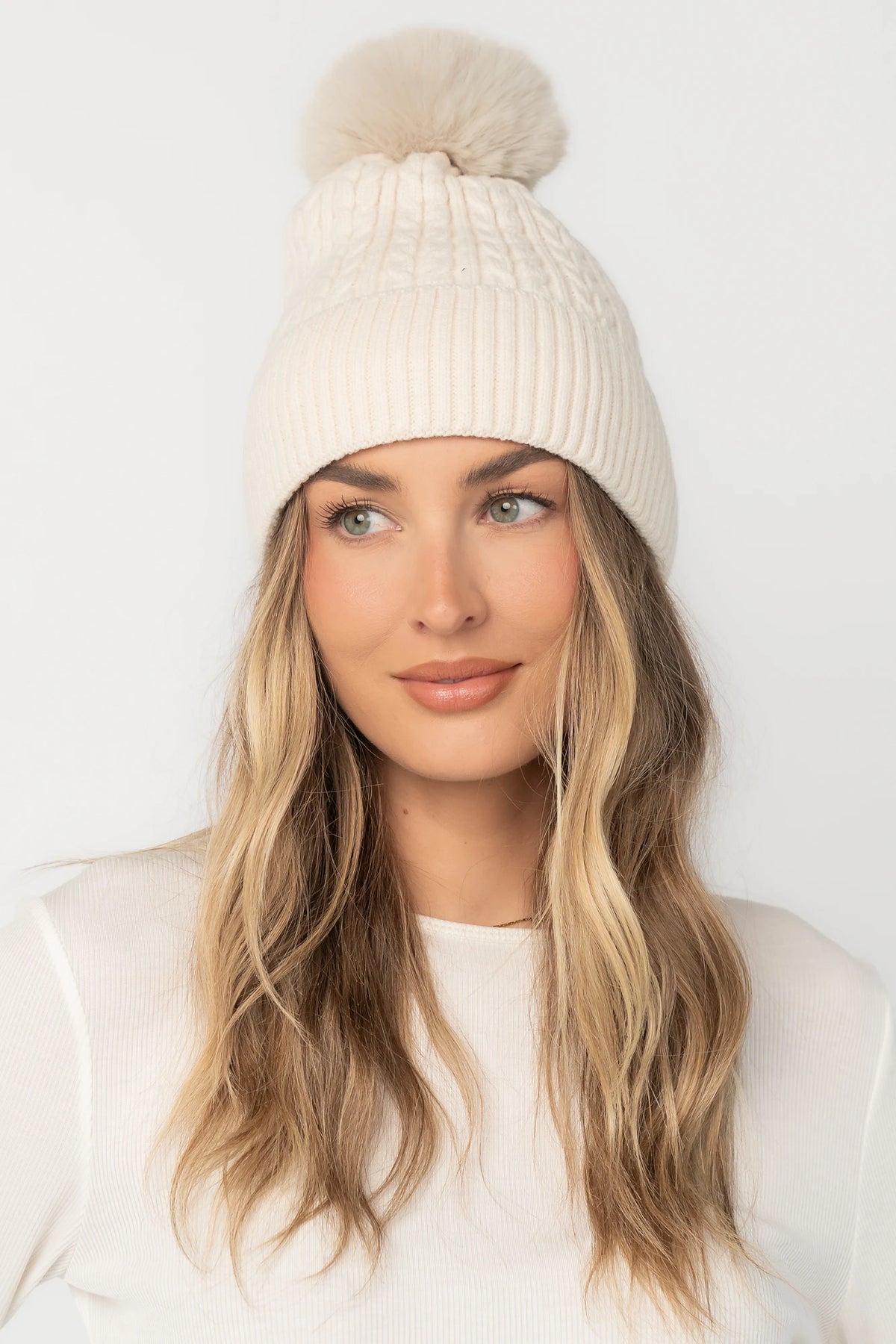 Lake Cable Knit Pom Beanie in Ivory with cable knit texture, faux fur pom, and fold-over ribbed cuff.