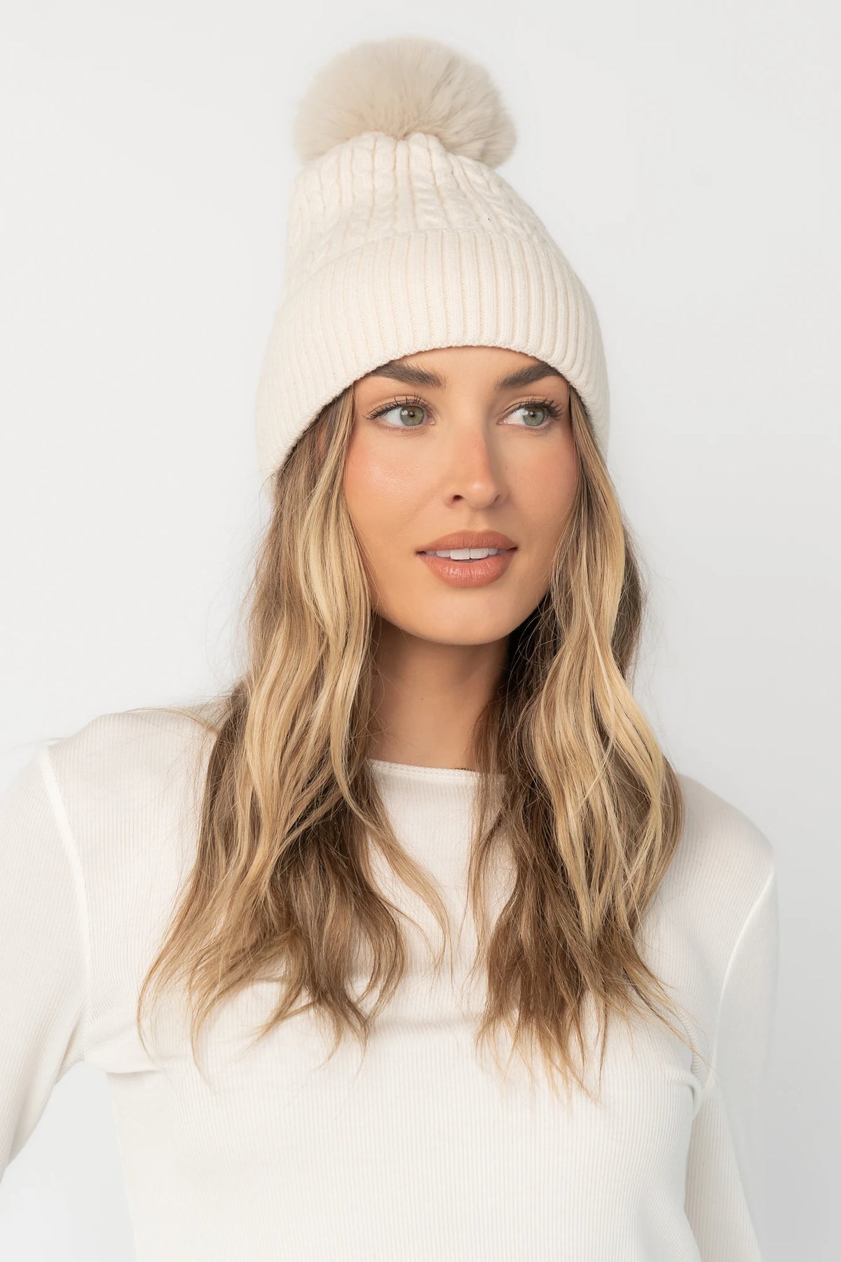 Lake Cable Knit Pom Beanie in Ivory with cable knit texture, faux fur pom, and fold-over ribbed cuff.