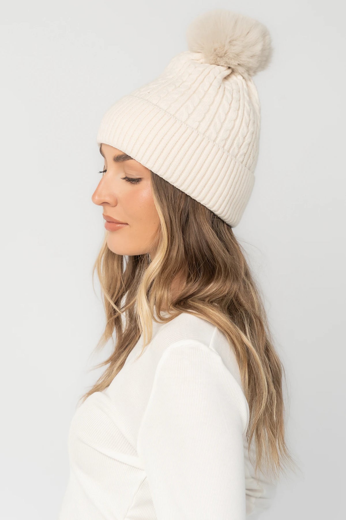 Lake Cable Knit Pom Beanie in Ivory with cable knit texture, faux fur pom, and fold-over ribbed cuff.
