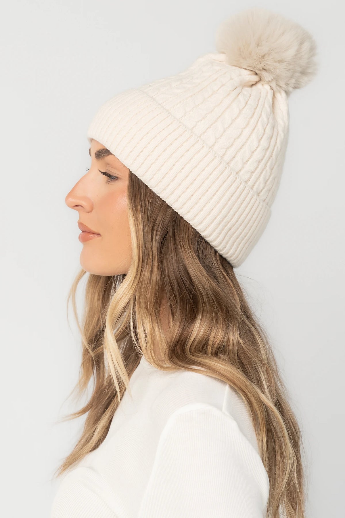 Lake Cable Knit Pom Beanie in Ivory with cable knit texture, faux fur pom, and fold-over ribbed cuff.