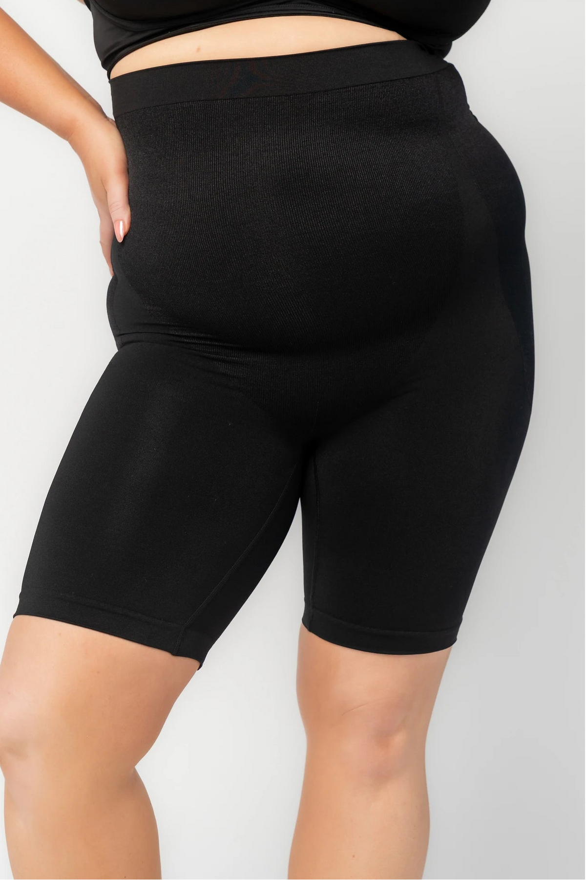 Model wearing black high-waisted shaping shorts with a seamless design and mid-thigh length.