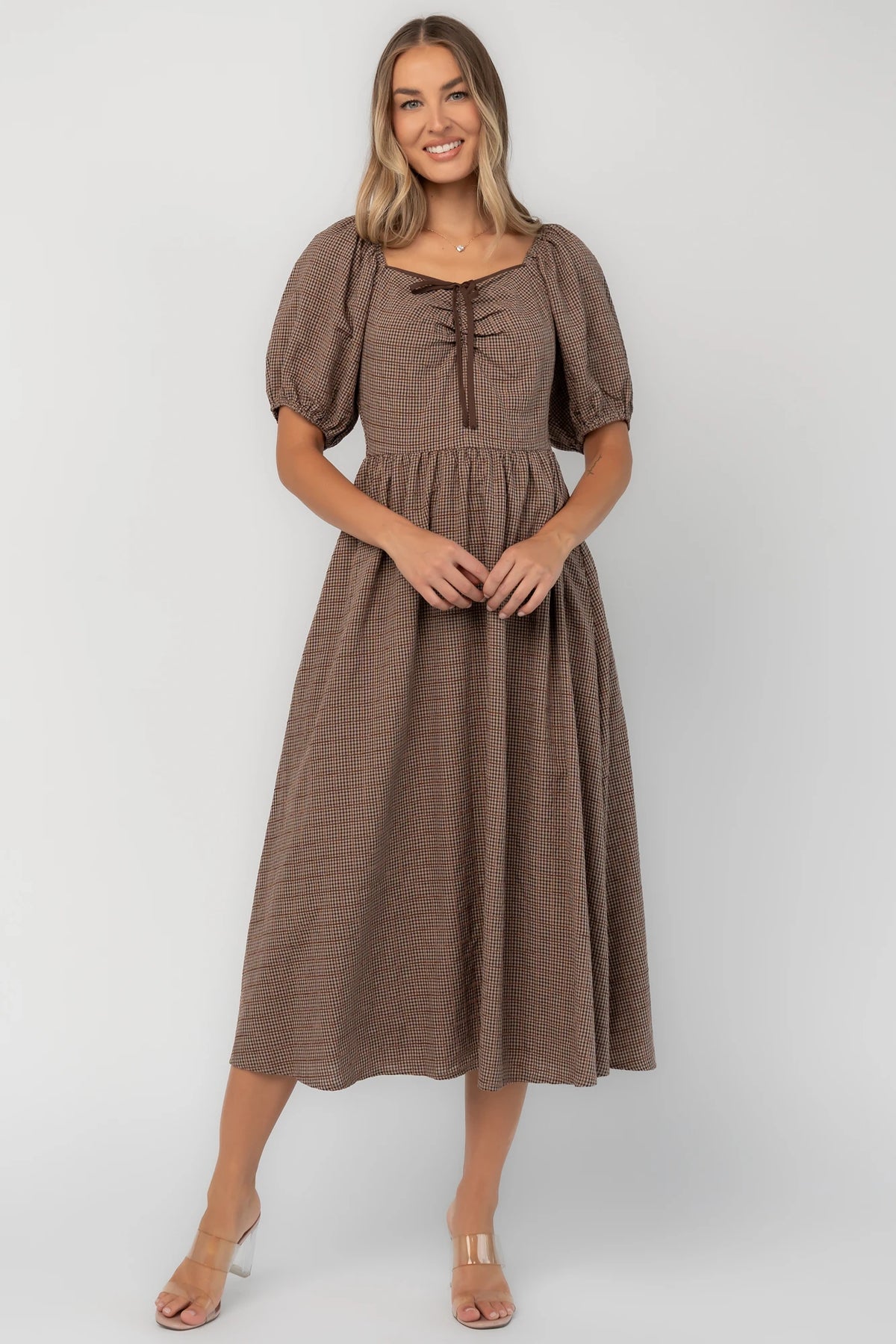 Mocha gingham midi dress with a square neckline, puff sleeves, smocked back, side pockets, and a flowing tiered skirt.