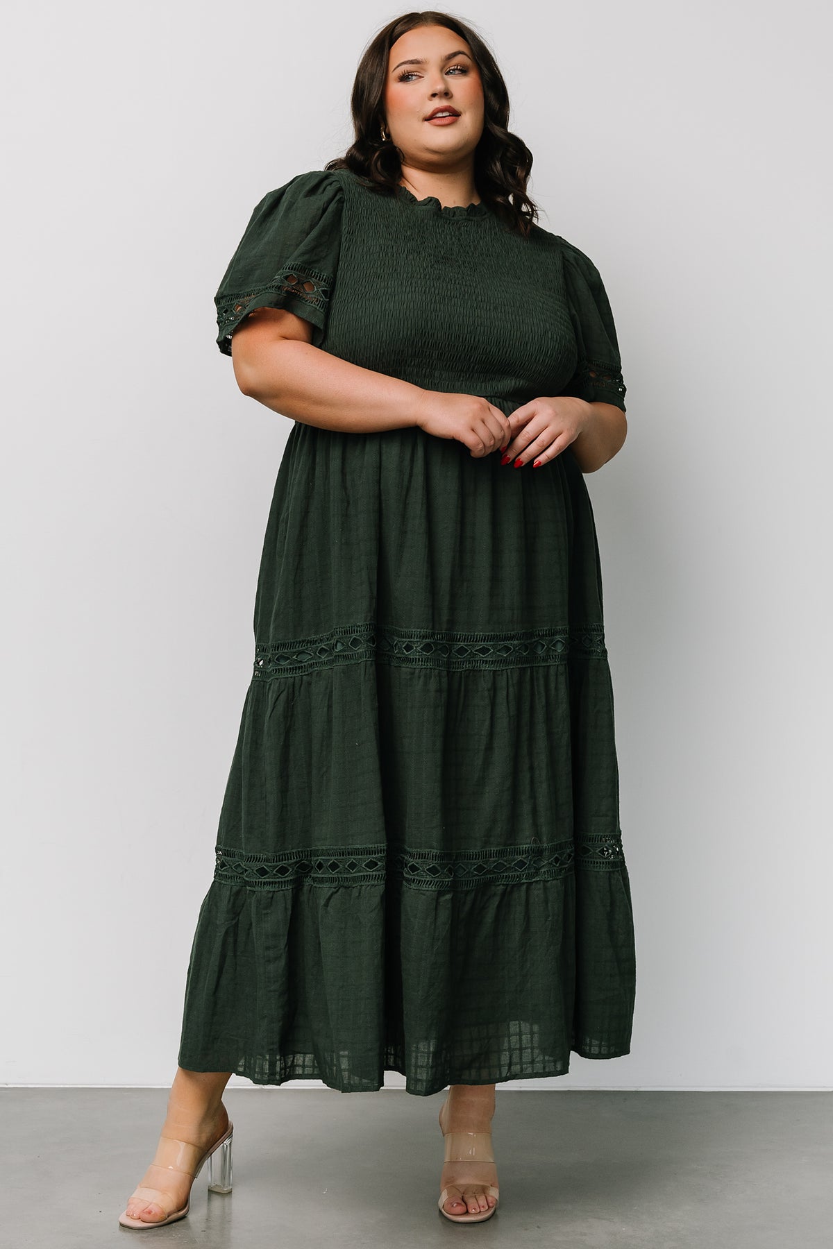 Front view of dark green maxi dress emphasizing lace texture, smocked chest, elastic waist, and flowing tiered skirt with subtle patterning.