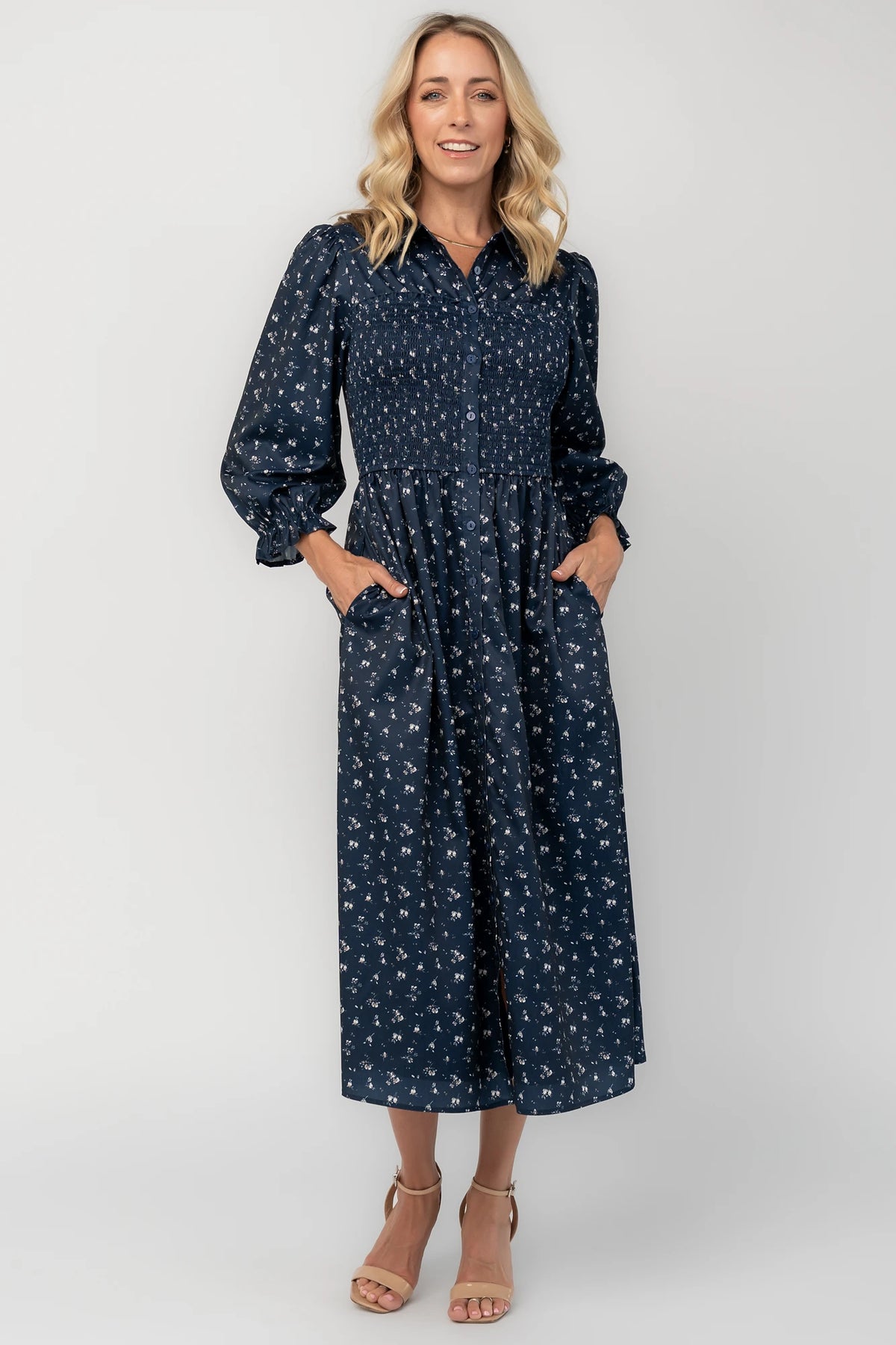 Navy floral button-down midi dress with a collared neckline, smocked bodice, three-quarter sleeves, elastic back waist, side pockets, and a flowing skirt.