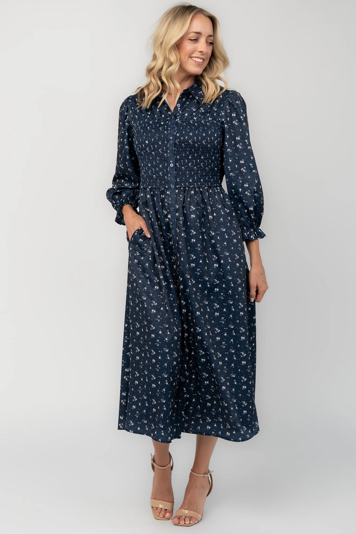 Navy floral button-down midi dress with a collared neckline, smocked bodice, three-quarter sleeves, elastic back waist, side pockets, and a flowing skirt.