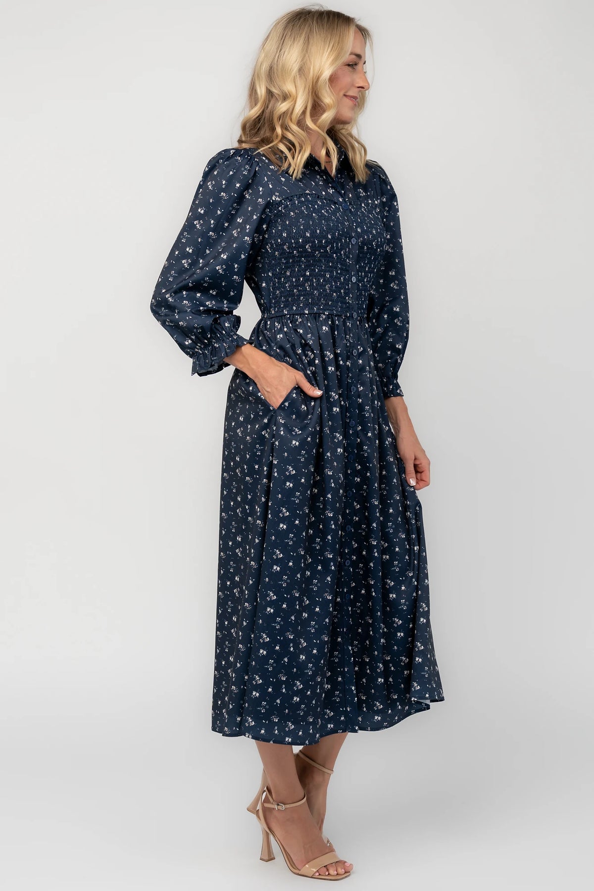 Navy floral button-down midi dress with a collared neckline, smocked bodice, three-quarter sleeves, elastic back waist, side pockets, and a flowing skirt.