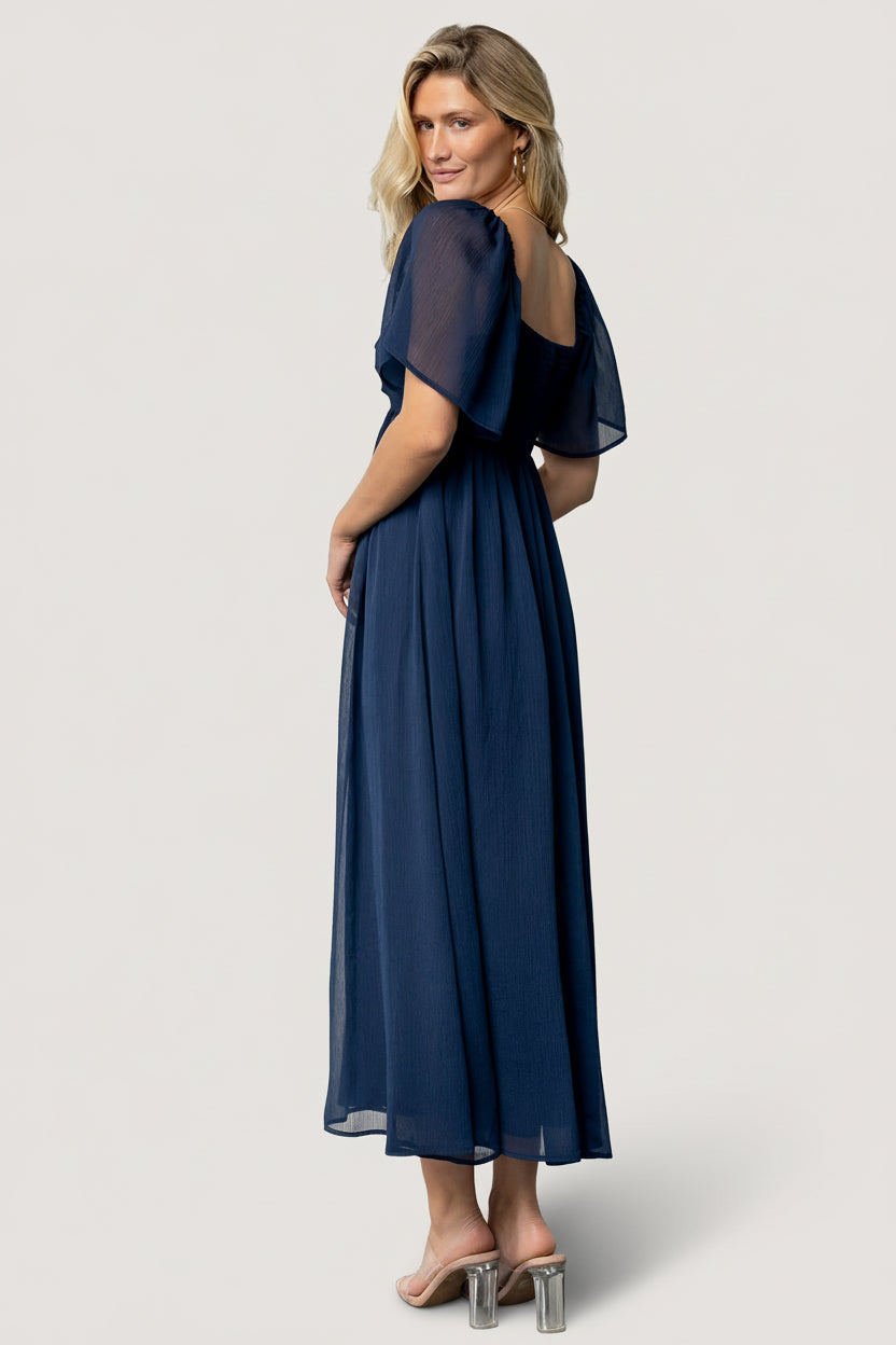 Rear view highlighting the smocked back panel and empire waist of the navy Nora Midi Dress, demonstrating flexible fit and subtle shaping.