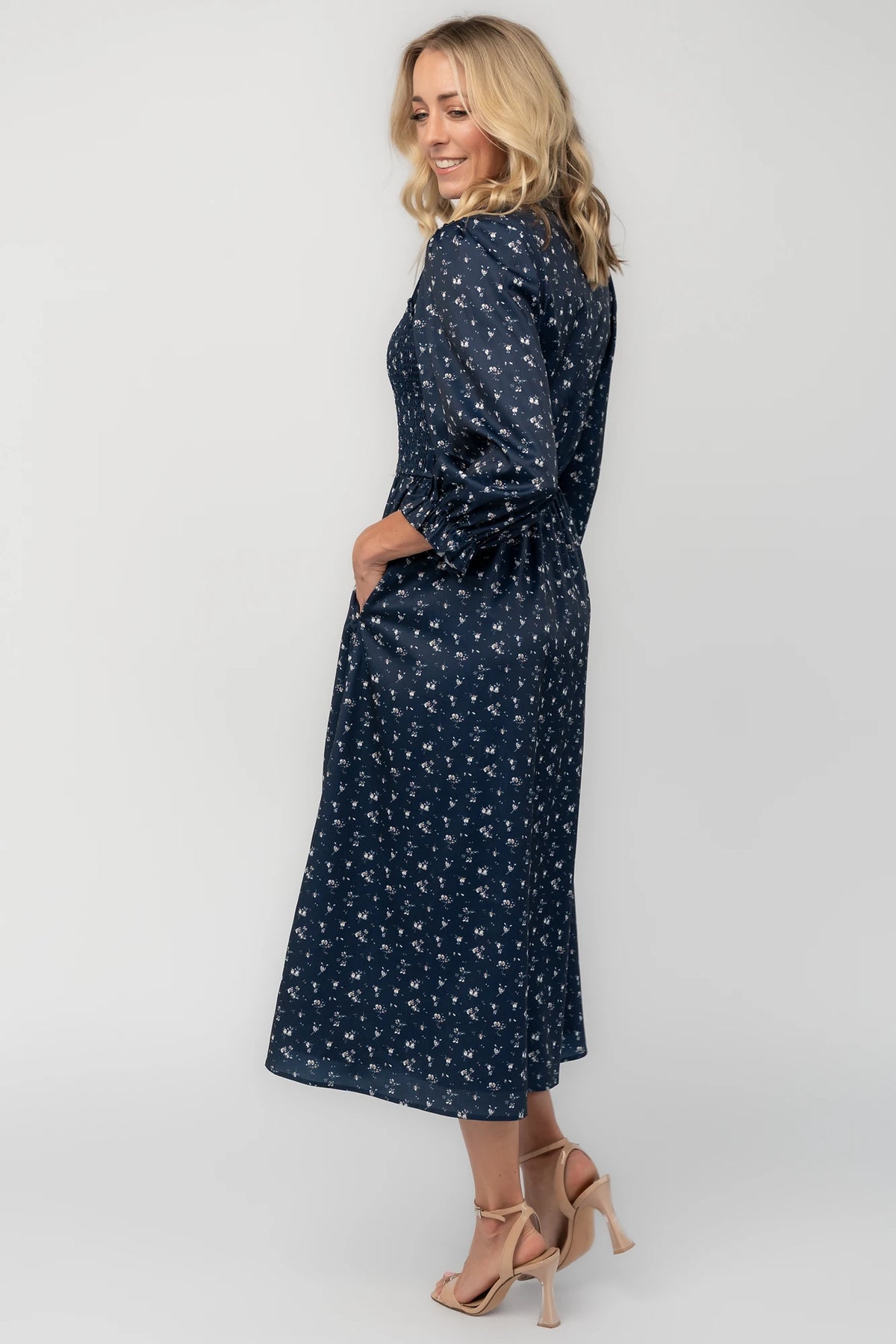 Navy floral button-down midi dress with a collared neckline, smocked bodice, three-quarter sleeves, elastic back waist, side pockets, and a flowing skirt.