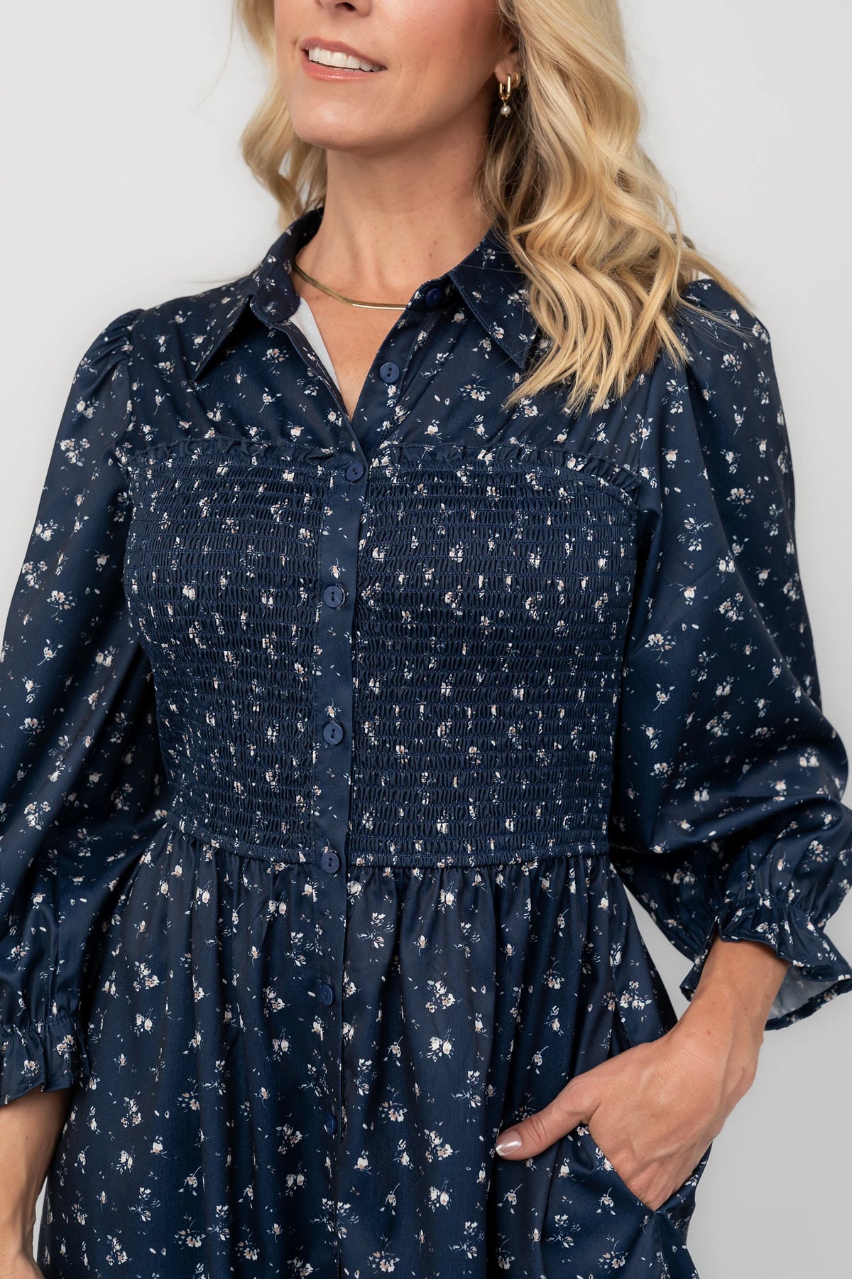 Navy floral button-down midi dress with a collared neckline, smocked bodice, three-quarter sleeves, elastic back waist, side pockets, and a flowing skirt.