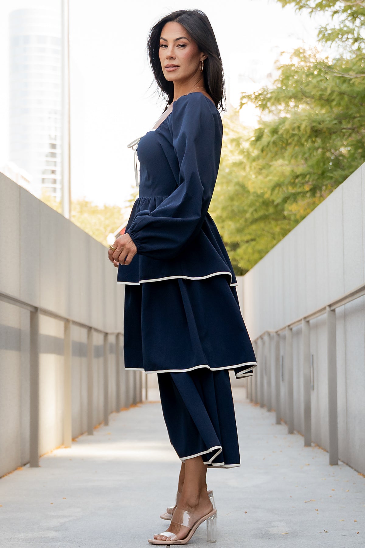 Styled outfit image of navy Barcelona dress paired with neutral sandals, showing midi length, sweetheart neckline, and ivory trim details.