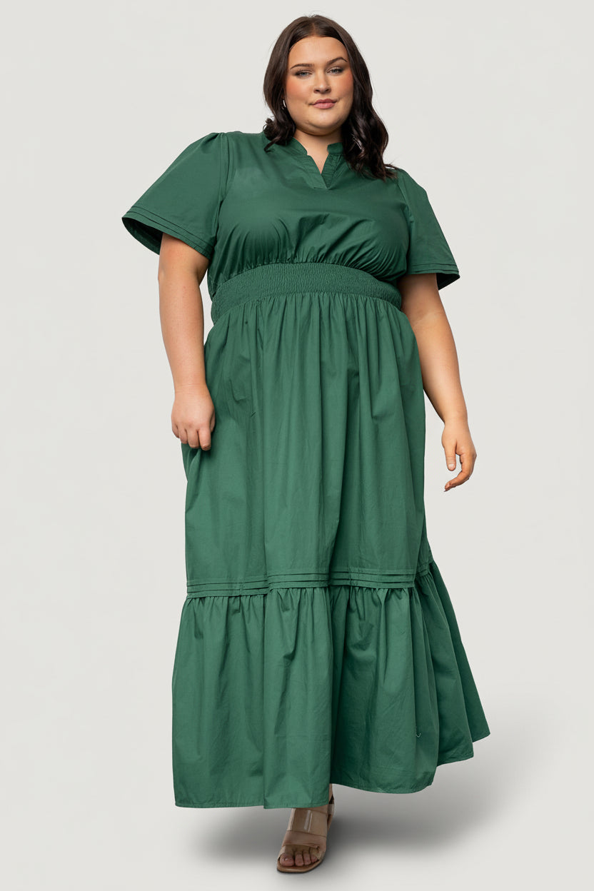 Three-quarter view of Vera Maxi Dress in emerald highlighting subtle layered sleeve details, fabric drape, and the dress length on a standing model.