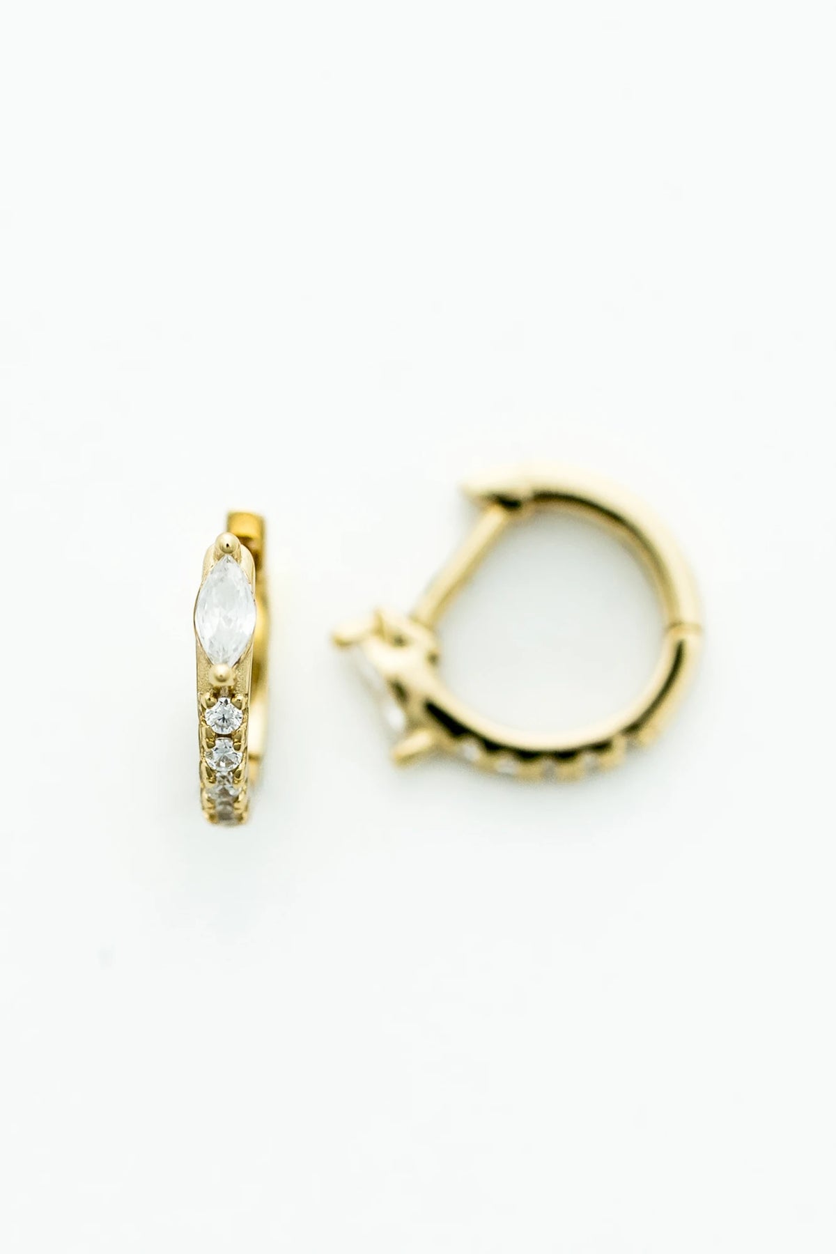 Petite gold huggie hoop earrings featuring a marquise-cut crystal accent and a row of sparkling stones along the front. 