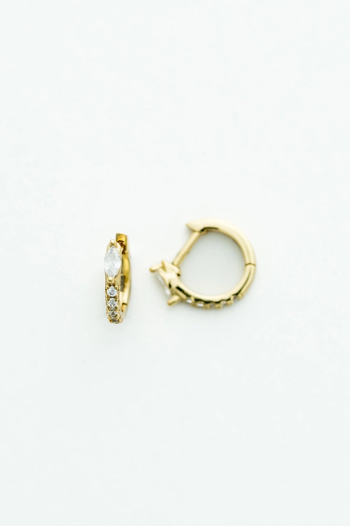 Petite gold huggie hoop earrings featuring a marquise-cut crystal accent and a row of sparkling stones along the front. 