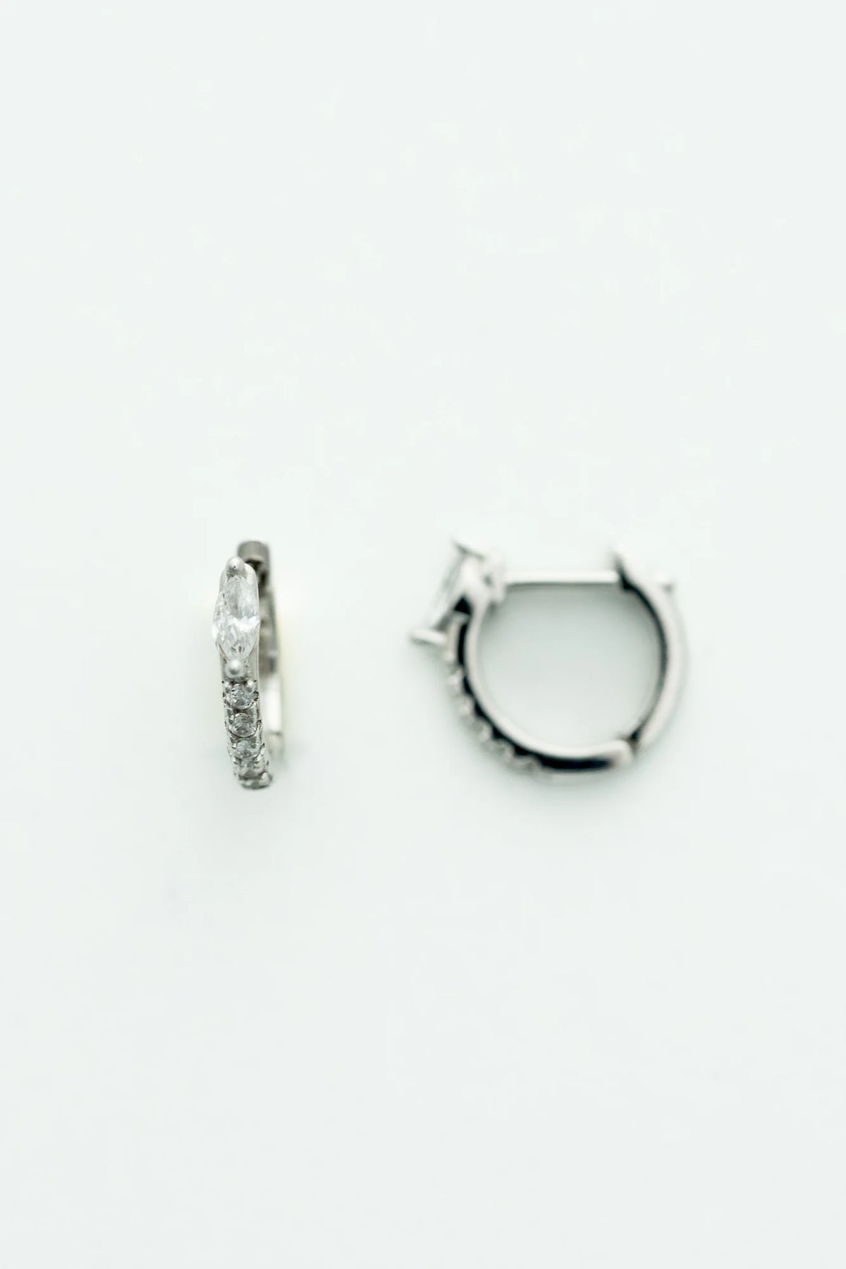 Petite sterling silver huggie hoop earrings featuring a marquise-cut crystal accent and a row of sparkling stones along the front. 
