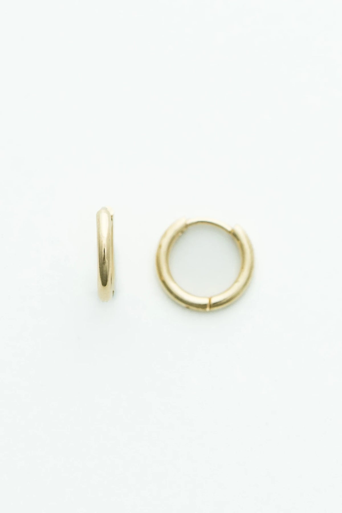 Polished gold-tone huggie hoop earrings featuring a smooth, minimalist finish.