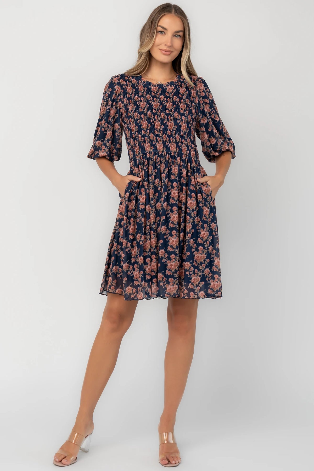 Navy floral mesh mini dress with a round neckline, elbow-length sleeves, smocked bodice, side pockets, and a flowy skirt.
