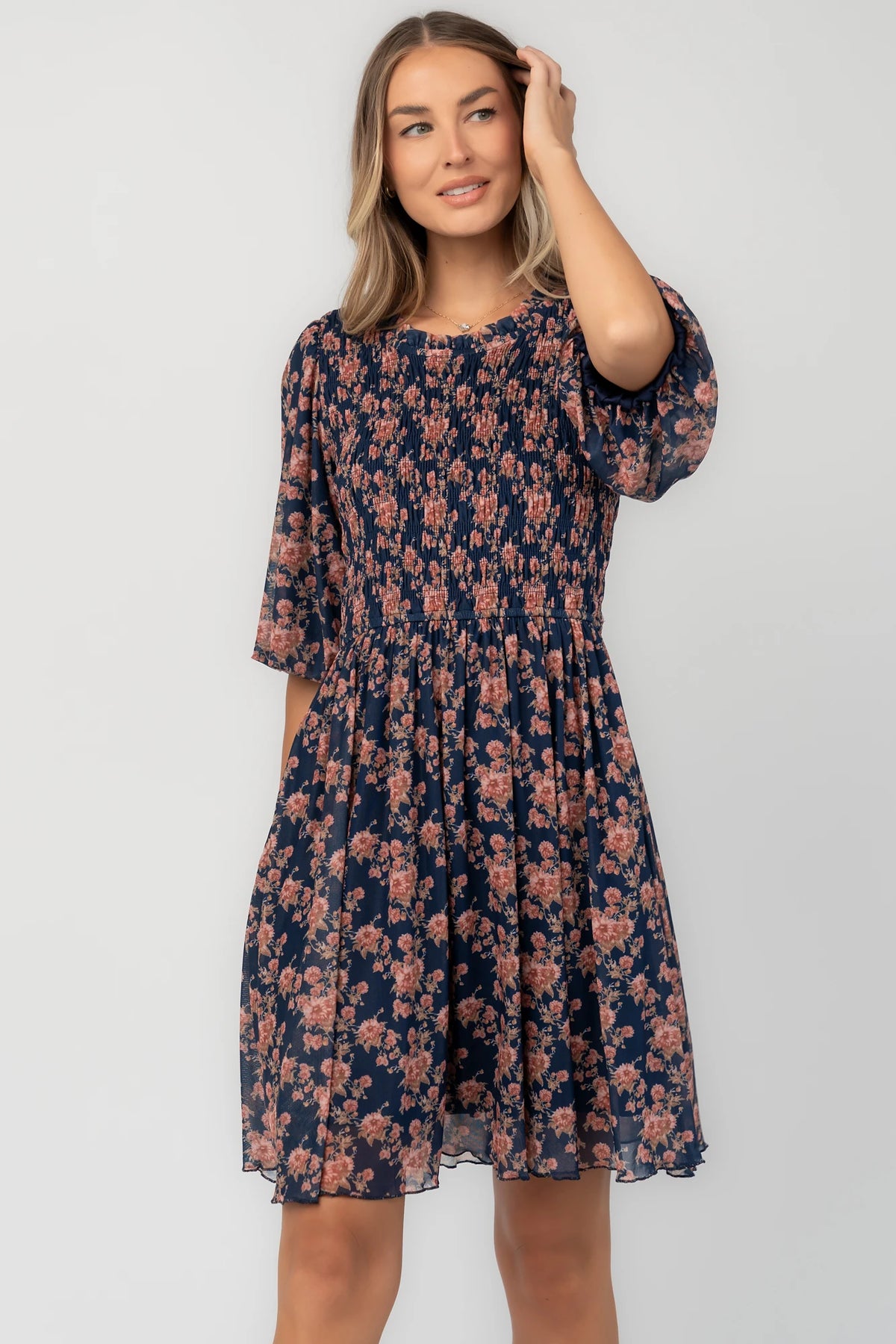 Navy floral mesh mini dress with a round neckline, elbow-length sleeves, smocked bodice, side pockets, and a flowy skirt.