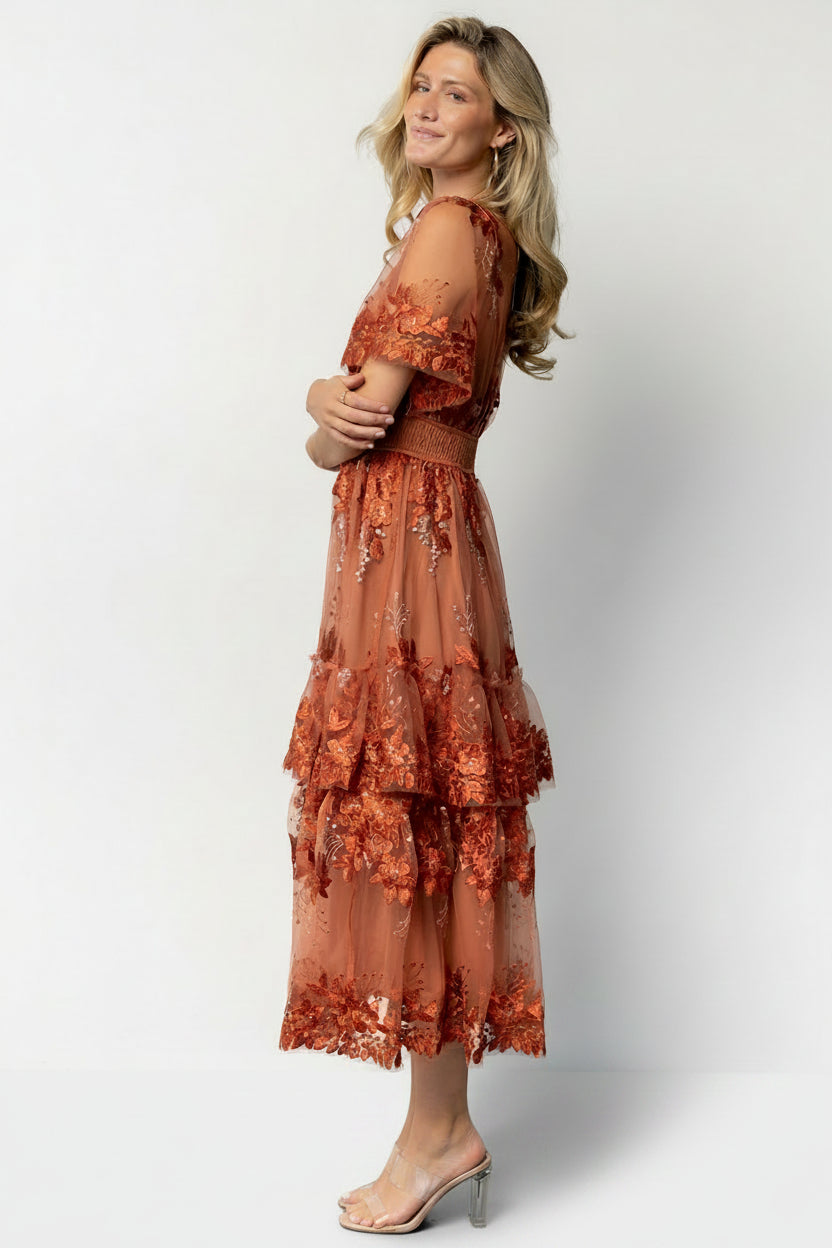 Model seated in the Lotte rust embroidered midi dress illustrating skirt drape, movement, and smocked waist detail.