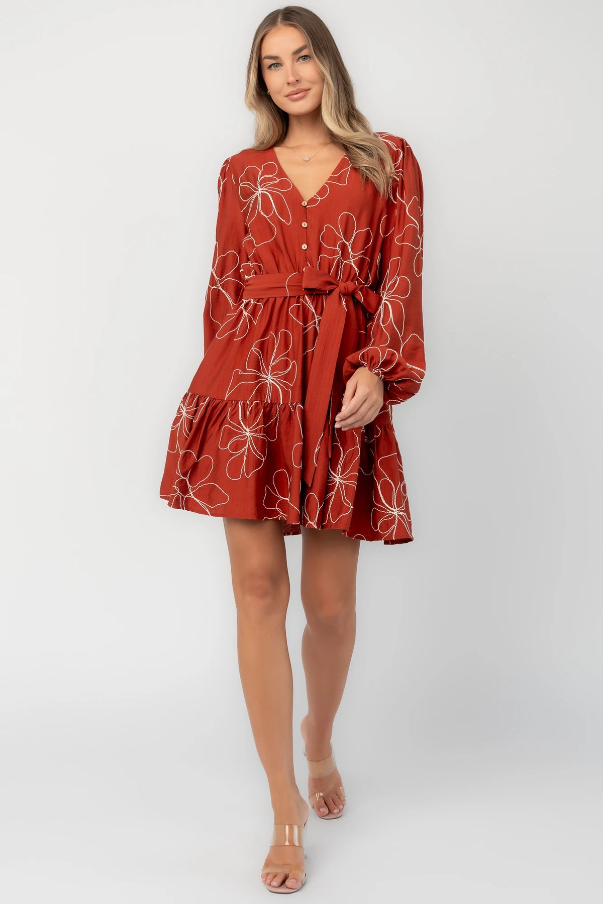 Rust floral mini dress with a V-neckline, button-front bodice, long balloon sleeves, elastic waistband with a self-tie sash, tiered ruffle hem, and side pockets.