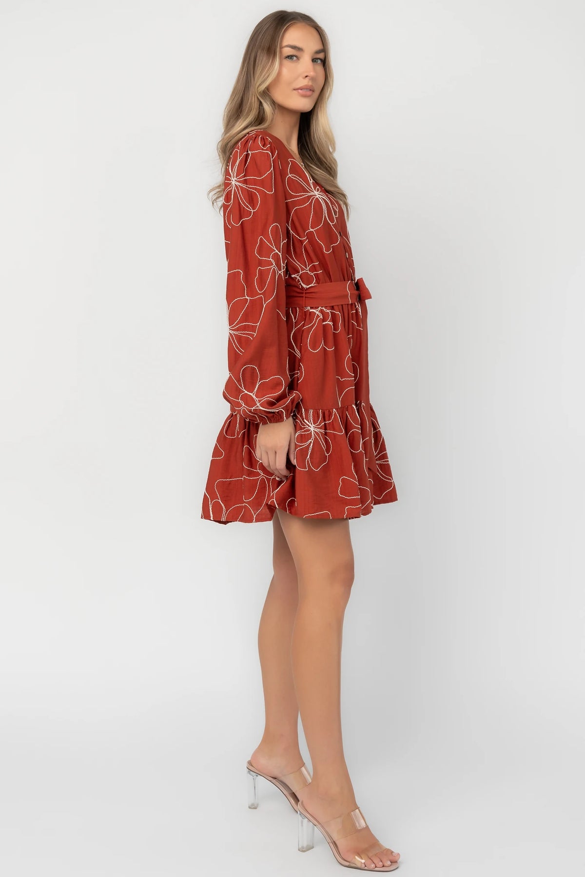 Rust floral mini dress with a V-neckline, button-front bodice, long balloon sleeves, elastic waistband with a self-tie sash, tiered ruffle hem, and side pockets.