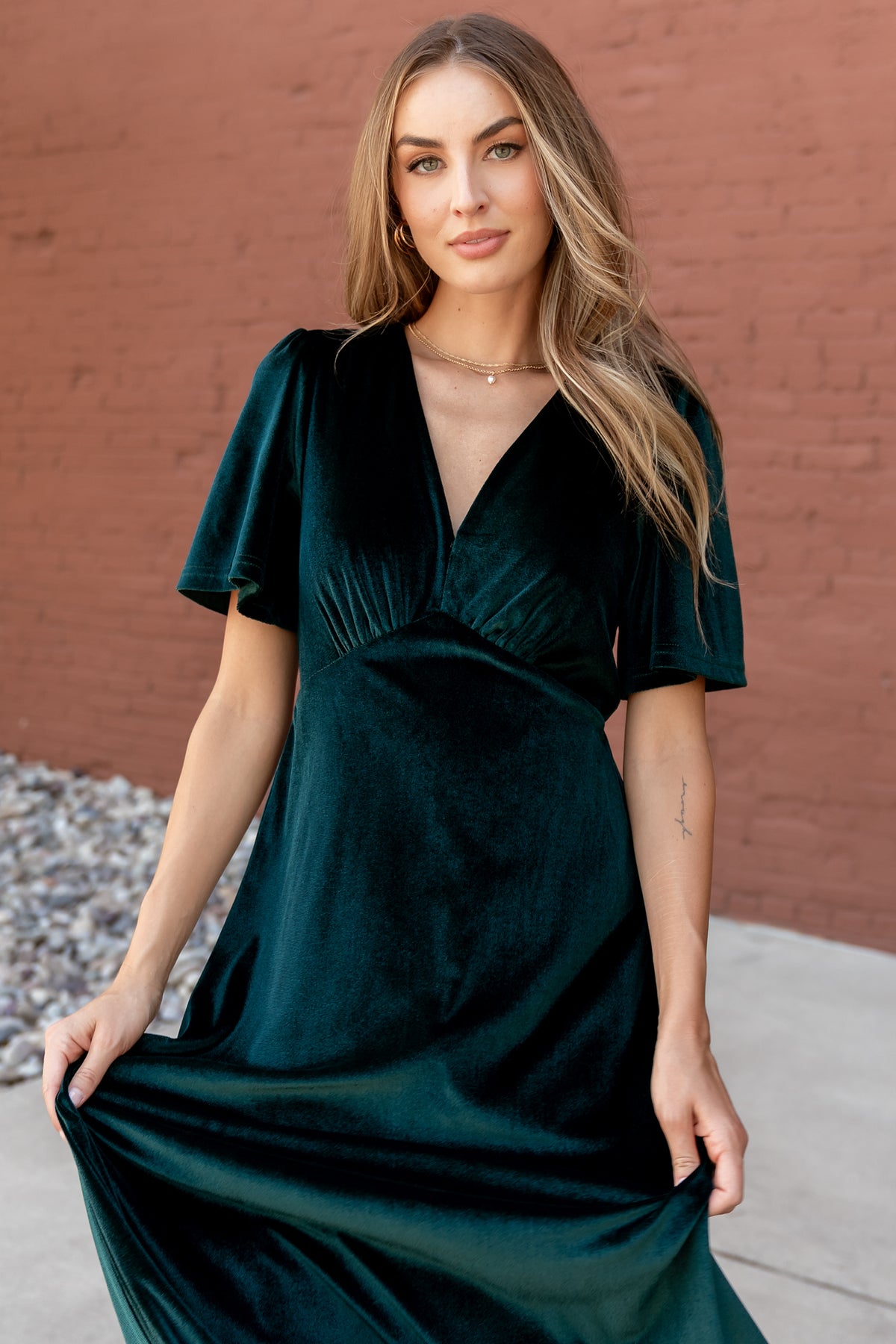 Three-quarter view of the emerald velvet Vivian maxi dress showing flutter sleeve detail, side drape, and flowing movement.