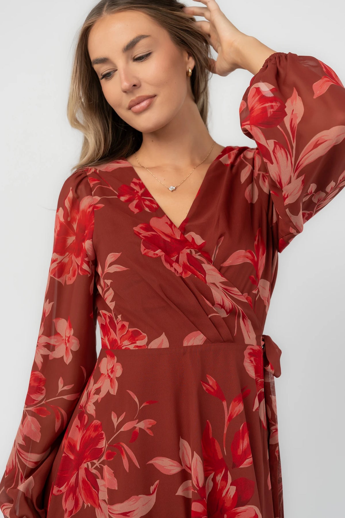 Rust multi floral chiffon maxi dress with a faux wrap neckline, long balloon sleeves, adjustable waist tie, and a high-low skirt.