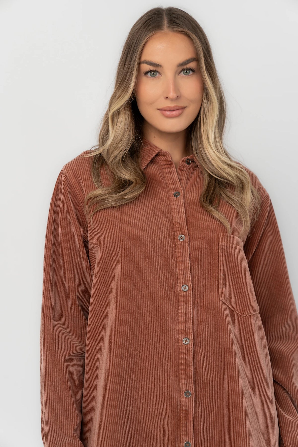 Dusty clay corduroy button-front shirt jacket with a collared neckline, oversized fit, chest pocket, long sleeves, and a rounded high-low hem.
