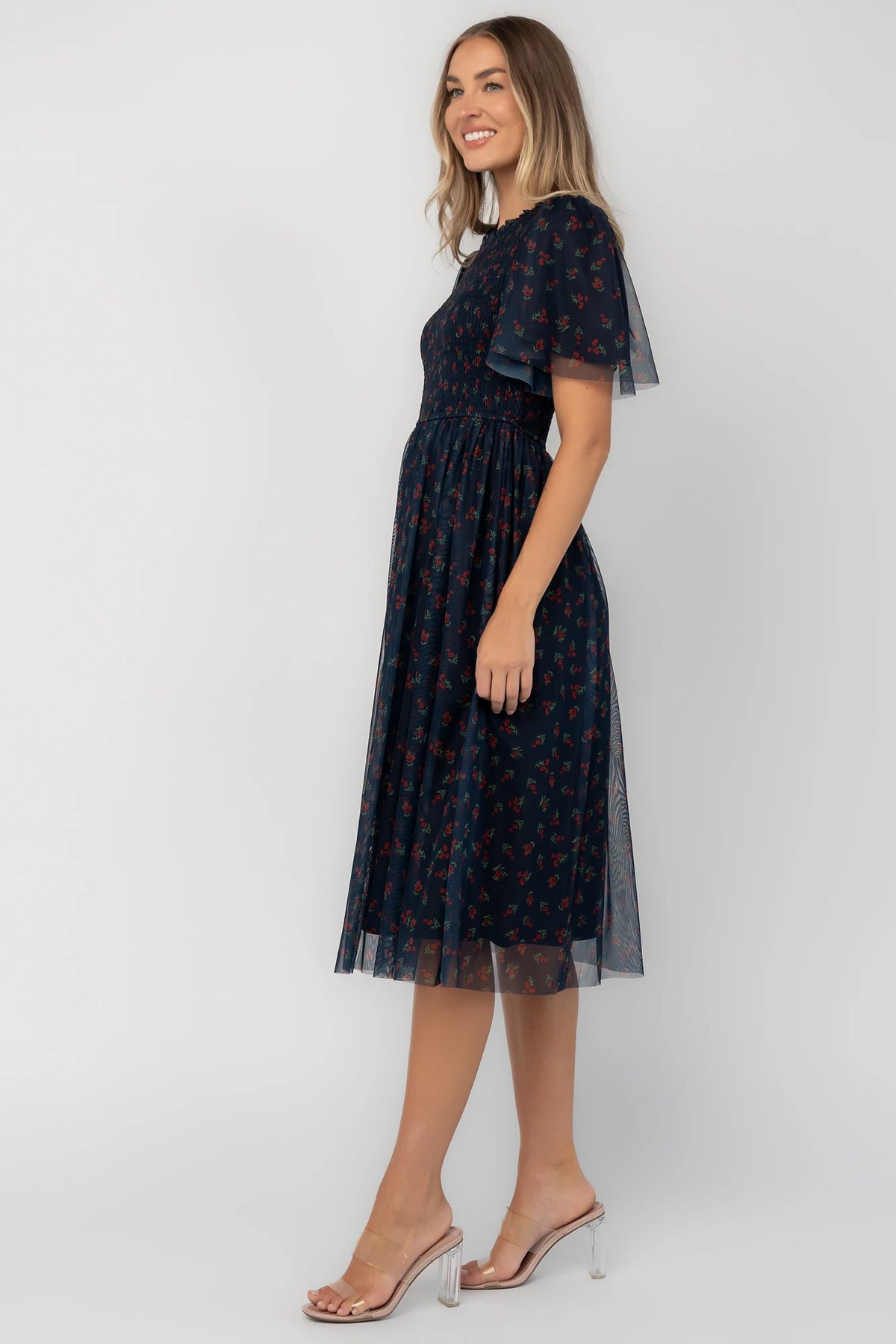 Navy floral mesh midi dress with a high ruffle neckline, flutter sleeves, full smocked bodice, and flowing midi skirt.