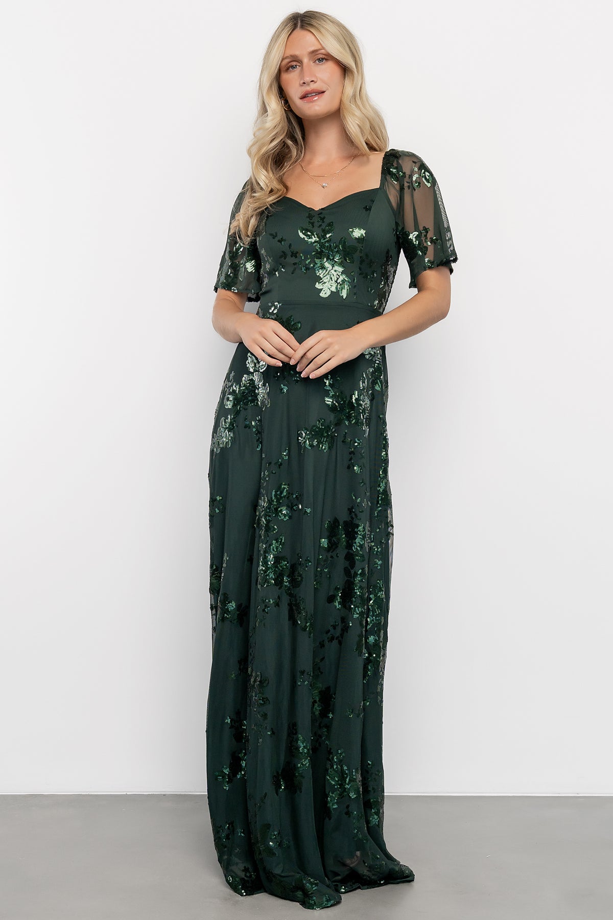 Model wearing the Karina dark green sequin maxi dress, full-length front view showing sweetheart neckline and flutter sleeves, polished look.