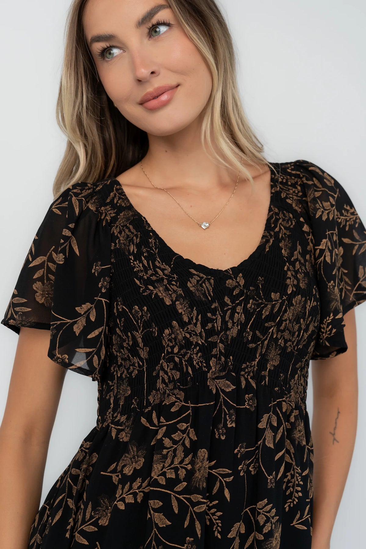 Black and gold chiffon maxi dress with a V-neckline, flutter sleeves, smocked bodice, empire waist, tiered skirt, and side pockets.