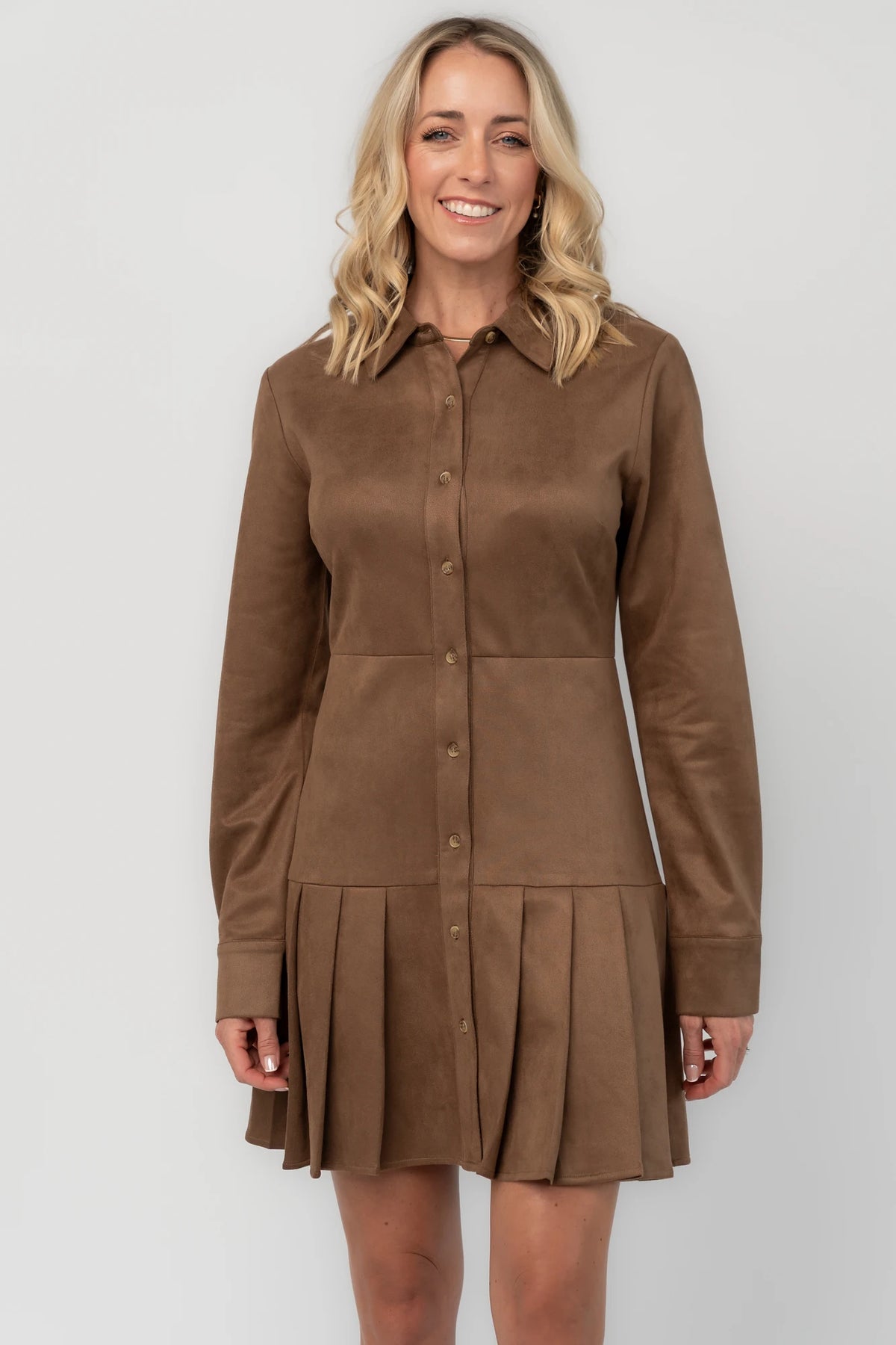 Coffee faux suede mini dress with a collared neckline, button-front closure, long sleeves, fitted waist, and pleated skirt.