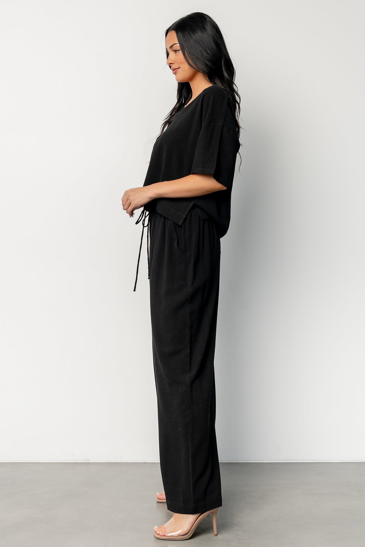 Side view highlighting the pants' wide leg, raw hem, and hidden side pockets on the black Timbre Matching Set.