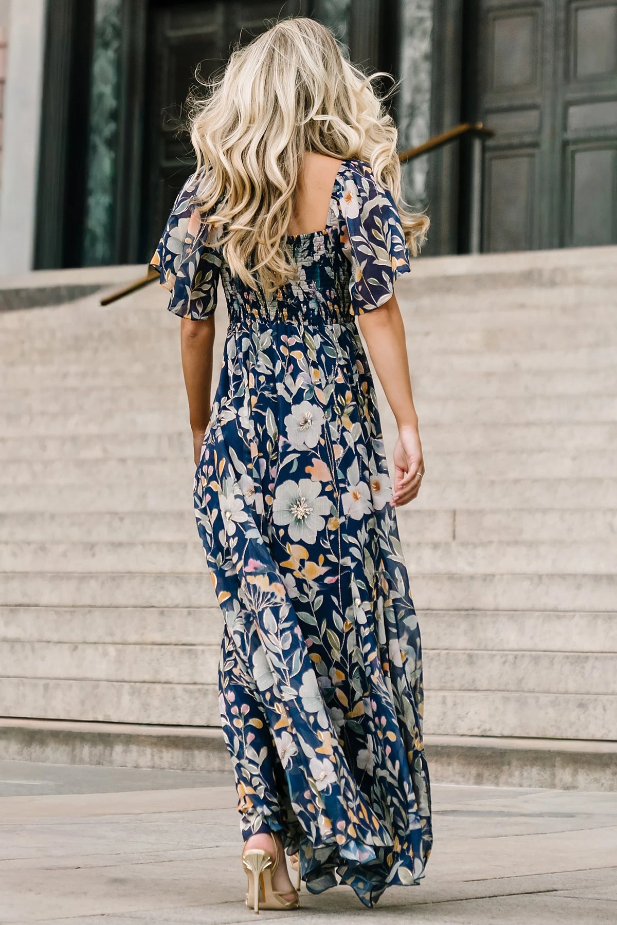 Navy floral chiffon maxi dress with a sweetheart neckline, knot detail, flutter sleeves, smocked back bodice, and a flowing tiered skirt.