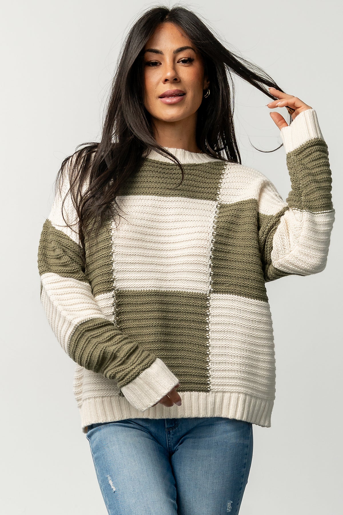 Lifestyle image of Jayda checkered sweater in cream and olive on model, capturing movement, relaxed fit, and textured ribbed edges.