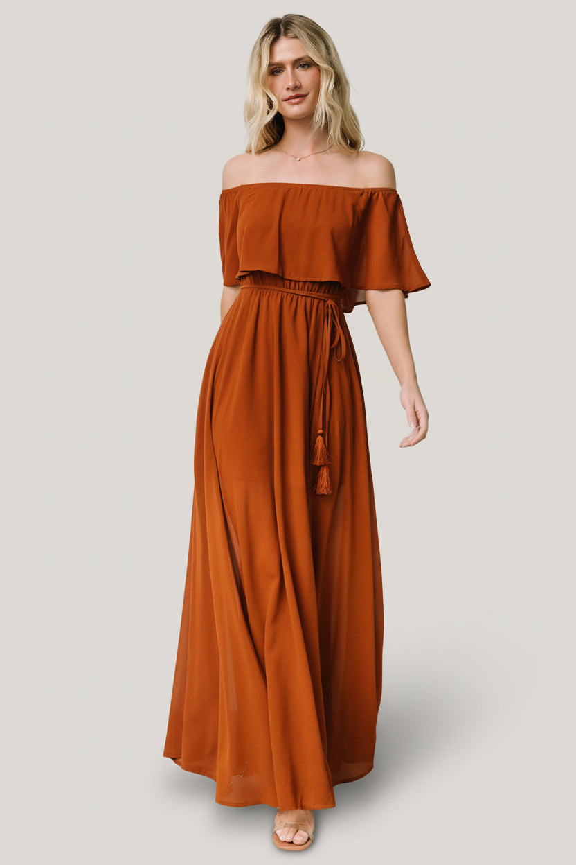 Front view of a model wearing a Spice off-shoulder maxi dress with elastic neckline, self-tie tassel belt, and flowing skirt.