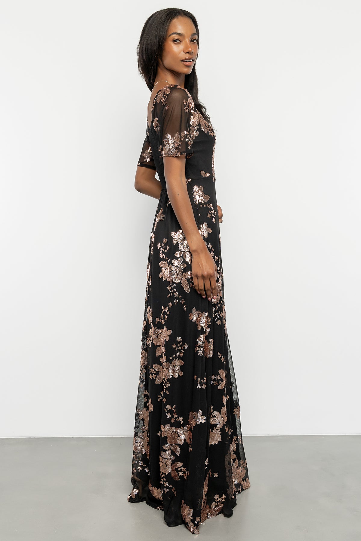Studio shot of full-length black and gold sequin maxi dress on model, showcasing silhouette and floor-skimming hemline.