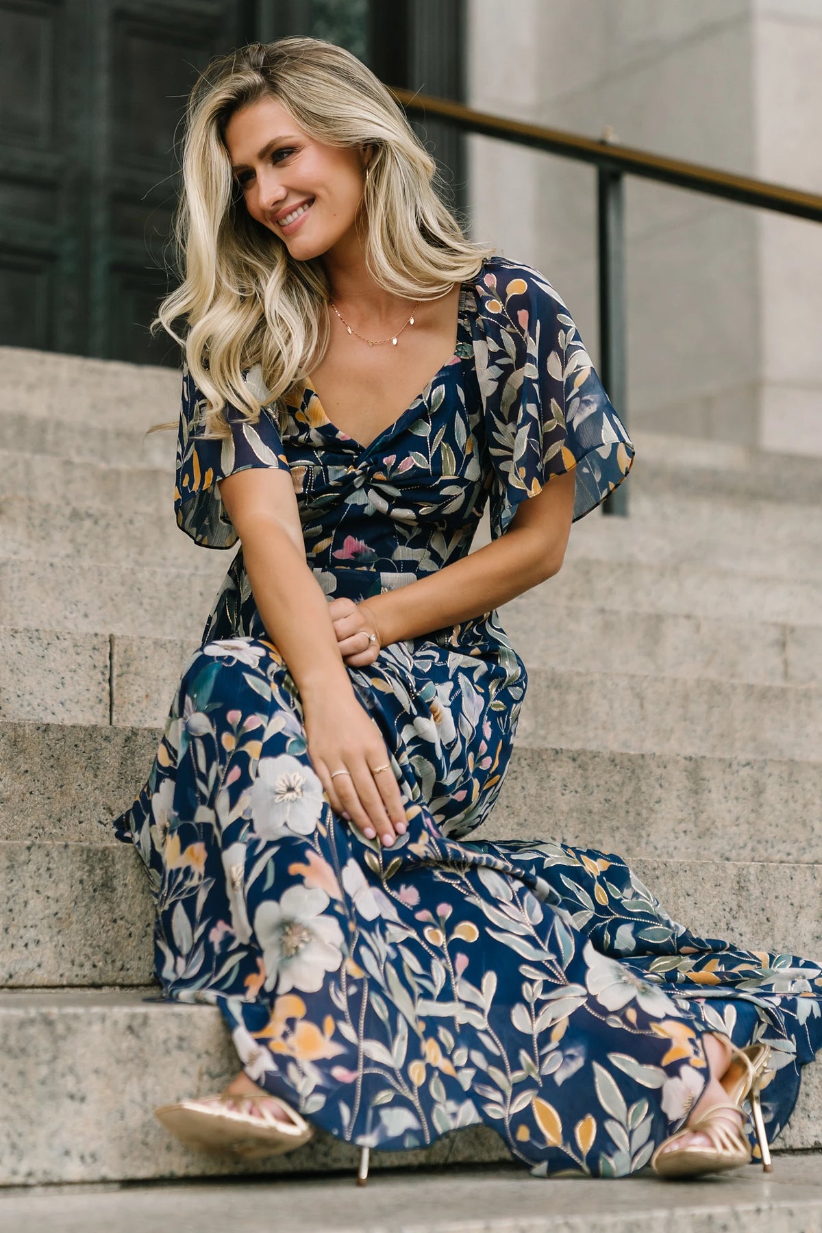 Navy floral chiffon maxi dress with a sweetheart neckline, knot detail, flutter sleeves, smocked back bodice, and a flowing tiered skirt.