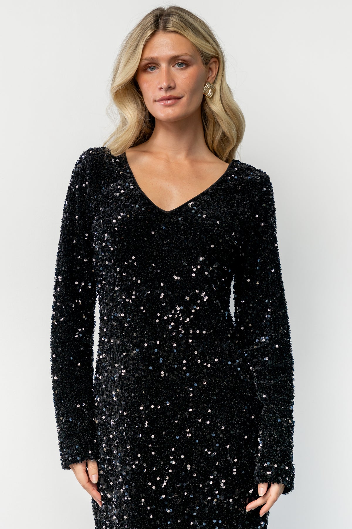 Three-quarter side view of the Mira black sequin dress showing straight fit silhouette, long sleeve detail, and short skirt length.