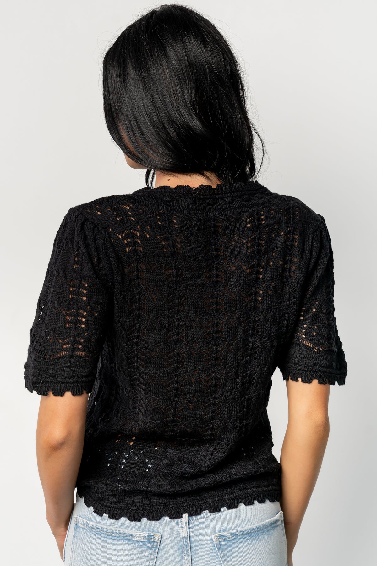 Close-up detail of scalloped collar and open-knit crochet holes on the Serenity Knit Sweater Top in black, showing yarn texture and stitch pattern.