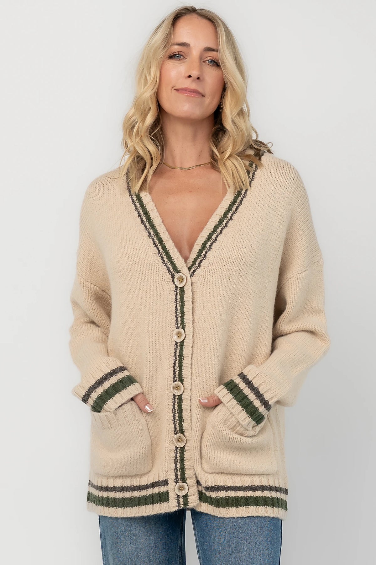 Oatmeal knit cardigan with a V-neckline, button-front closure, olive and charcoal striped trim, front patch pockets, and a relaxed fit.