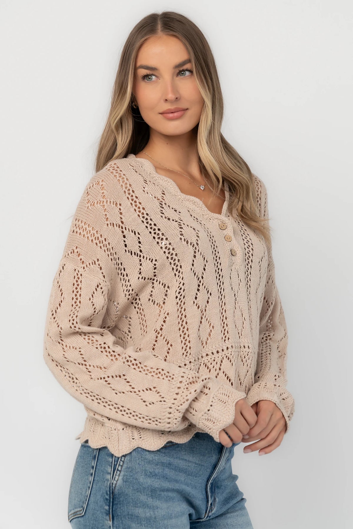 Oatmeal pointelle knit sweater with a scalloped henley neckline, functional button front, dropped shoulders, long sleeves, and a scalloped hem.