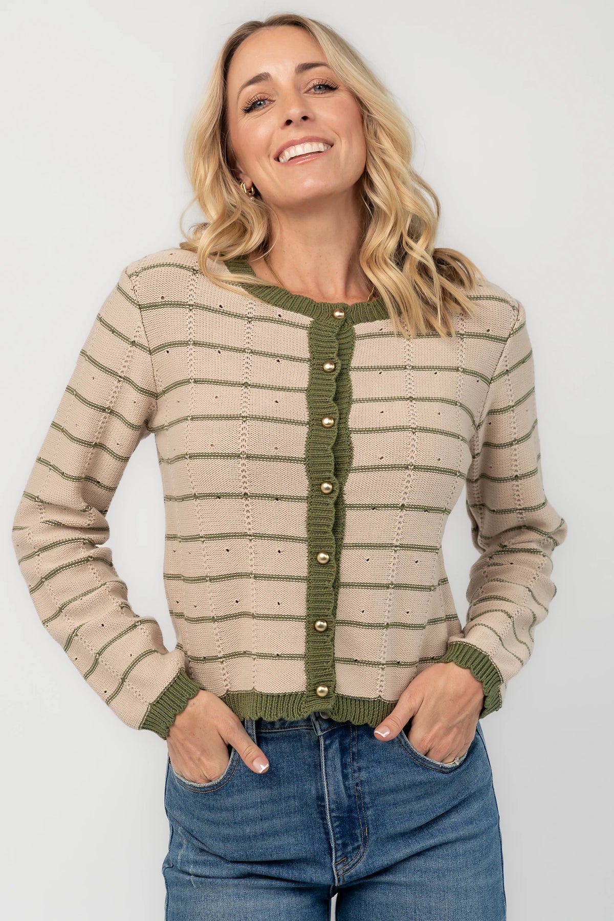 Beige pointelle knit cardigan with olive striped detailing, a round scalloped neckline, pearl-inspired button-front closure, long sleeves, and scalloped ribbed trim.