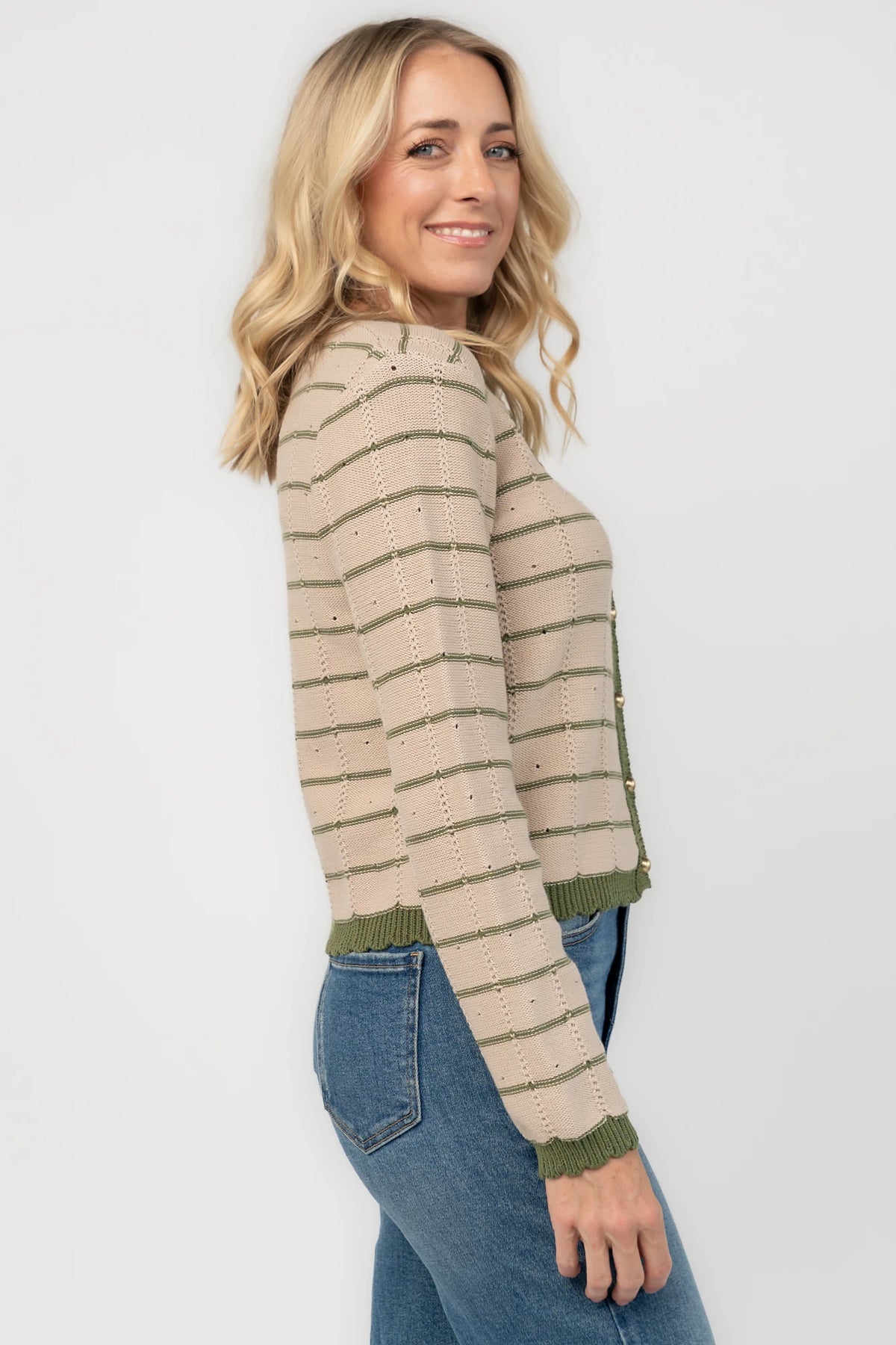Beige pointelle knit cardigan with olive striped detailing, a round scalloped neckline, pearl-inspired button-front closure, long sleeves, and scalloped ribbed trim.