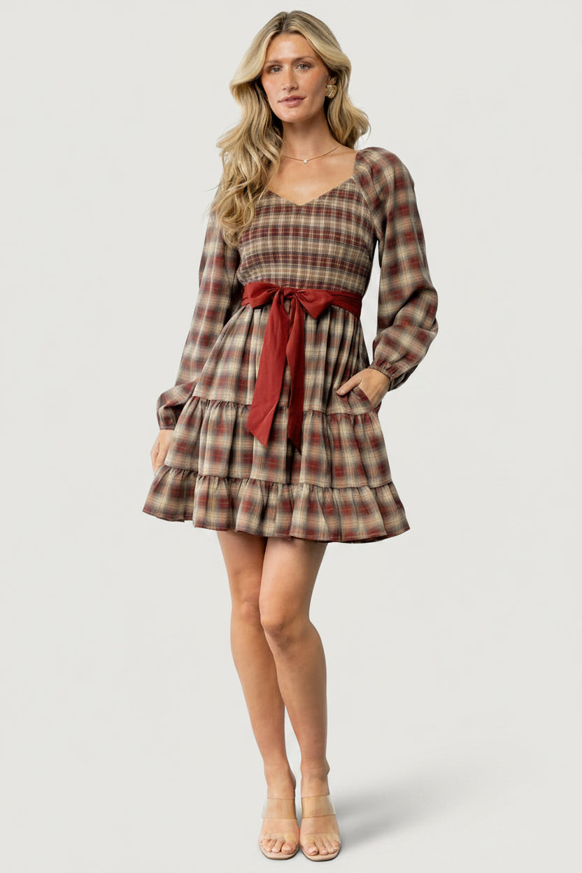 Front view of Stina Plaid Mini Dress on model showing V-neck smocked bodice, elastic cuffs, two-tiered short skirt, and waist sash.