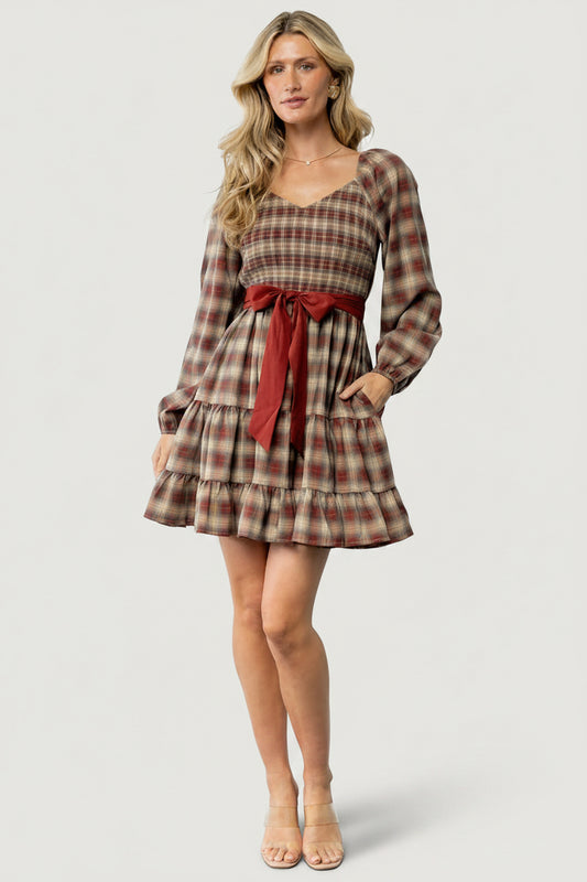 Front view of Stina Plaid Mini Dress on model showing V-neck smocked bodice, elastic cuffs, two-tiered short skirt, and waist sash.