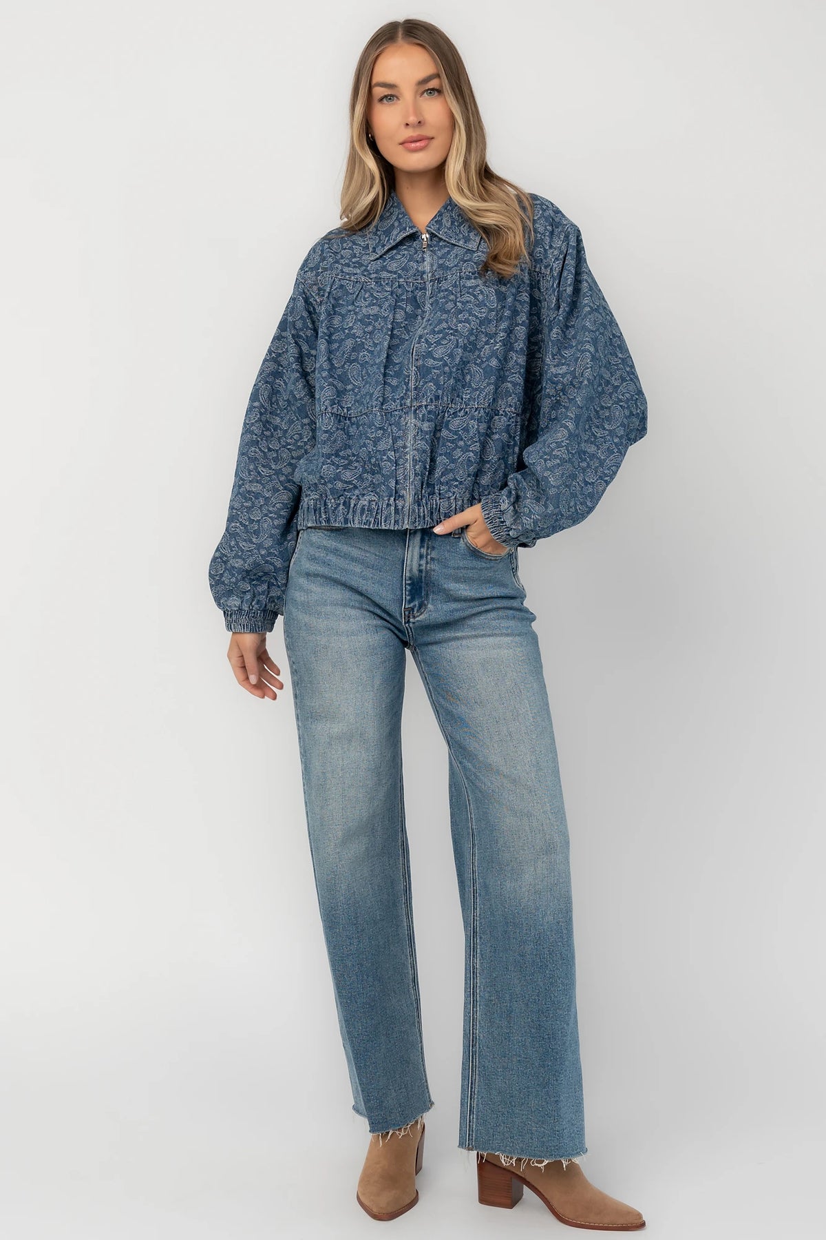Medium wash paisley print denim jacket with a collared neckline, front zipper closure, long sleeves, elastic hem, and side pockets.