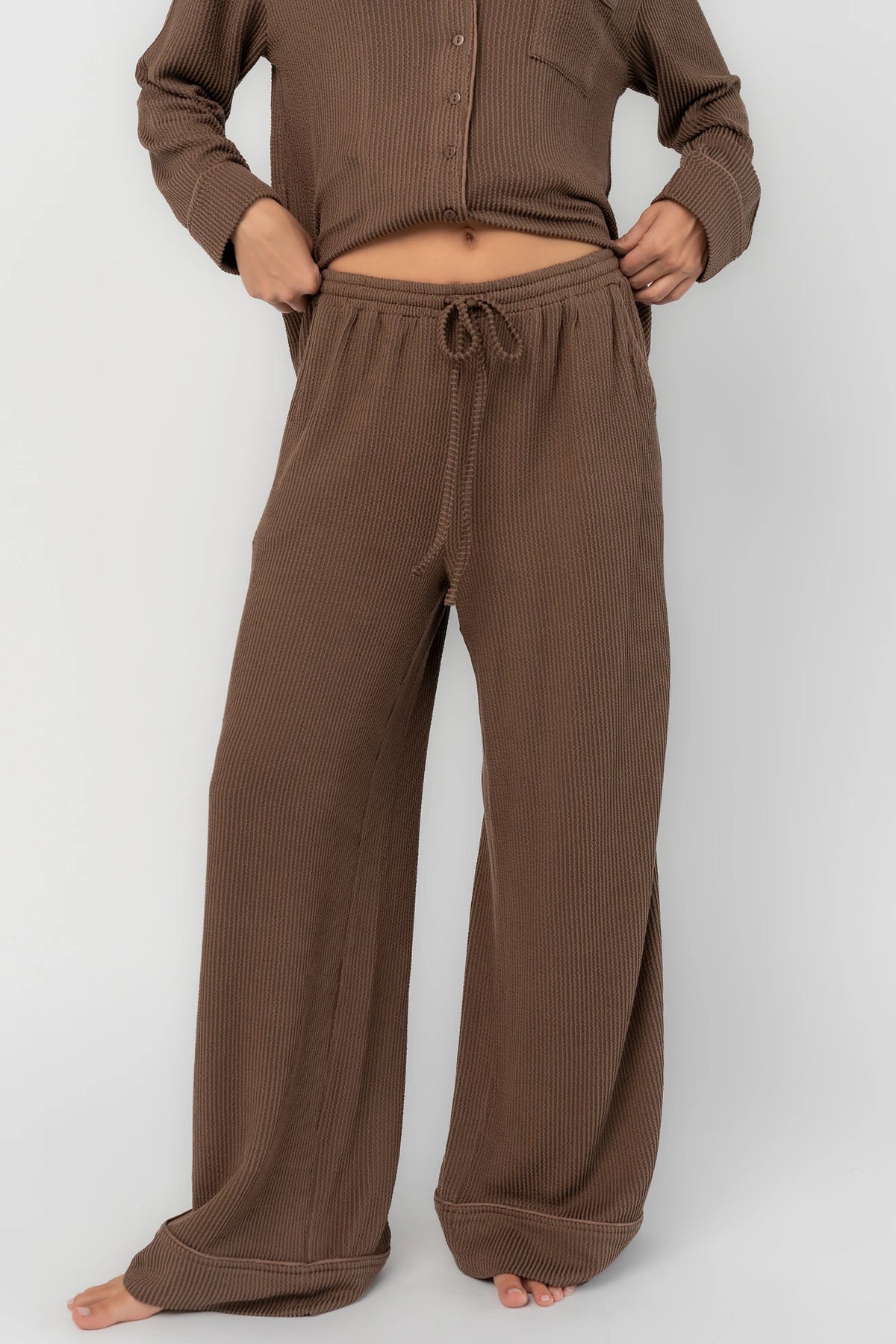 Brown ribbed pajama set with a button-front V-neck top, long sleeves, chest pocket, and wide-leg pants with an elastic drawstring waist.